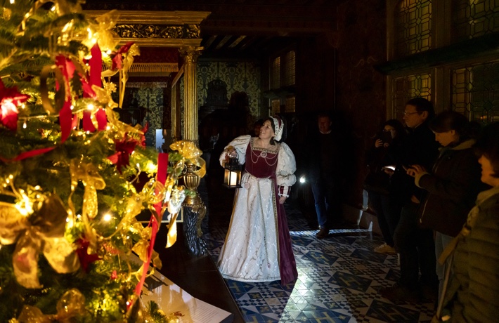 Une guide en costume d’époque présente une pièce du Château au public, à la lumière de lampes torche.
