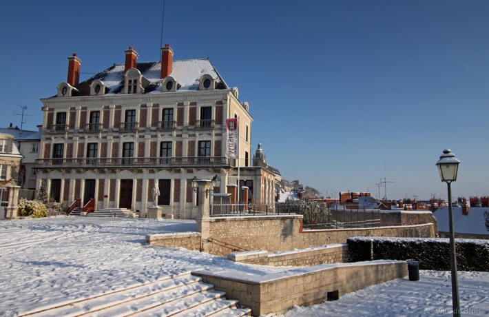 Photo de la façade de la Maison de la magie depuis la place du Château, sous la neige avec un ciel entièrement bleu.