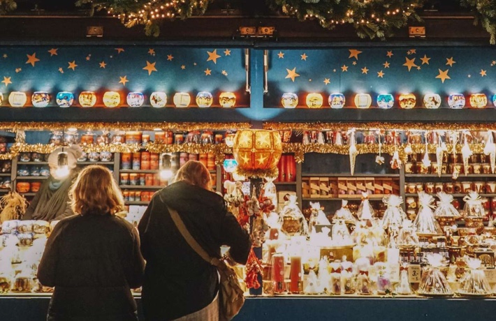 Deux personnes de dos se penchent sur un chalet de Noël débordant de lumières et de décorations.