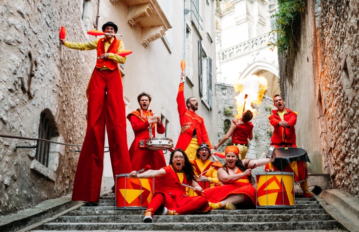 La troupe pose avec ses percussions. Parmi les 8 artistes, un s’apprête à jongler sur des échasses, et un autre crache du feu.