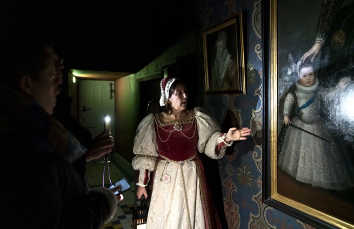 Une guide en costume d’époque présente un tableau du Château au public, à la lumière de lampes torche.