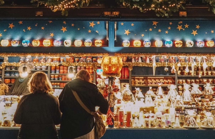 Deux personnes de dos se penchent sur un chalet de Noël débordant de lumières et de décorations.