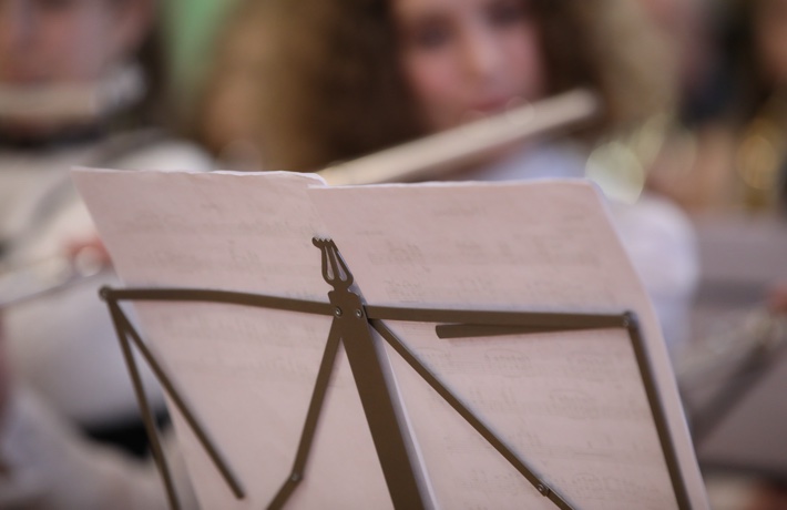 Un pupitre avec une partition de musique. En arrière-plan, floue, une personne joue de la flûte traversière à côté d’autres musiciennes et musiciens.