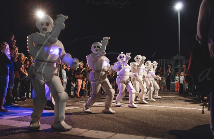 6 personnes en costume de robots blancs dansent au milieu de la foule, de nuit.